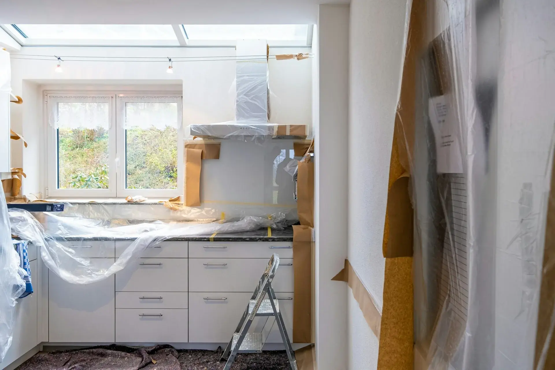 Kök under renovering med skyddsplast över köksluckor och en stege framme