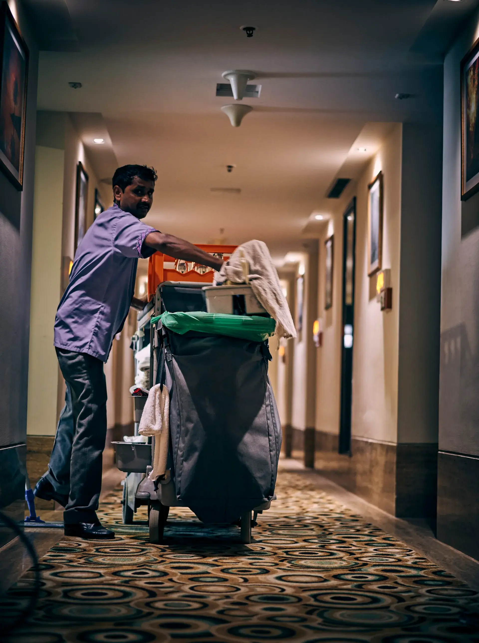 Lokalvårdare i arbetskläder som fyller på en städvagn i en korridor